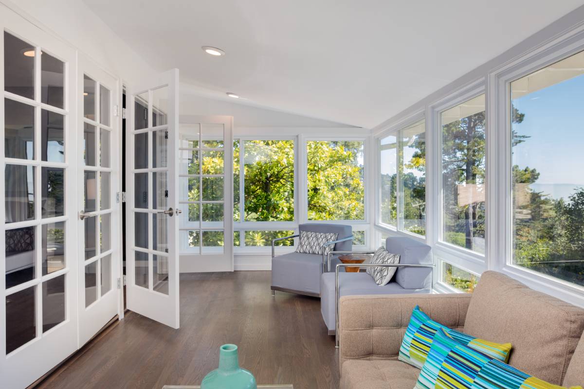 Bright white sunroom with large French doors and picture windows, overlooking a blue sky and full trees at Signature Shutters & Decor near Moraine, OH