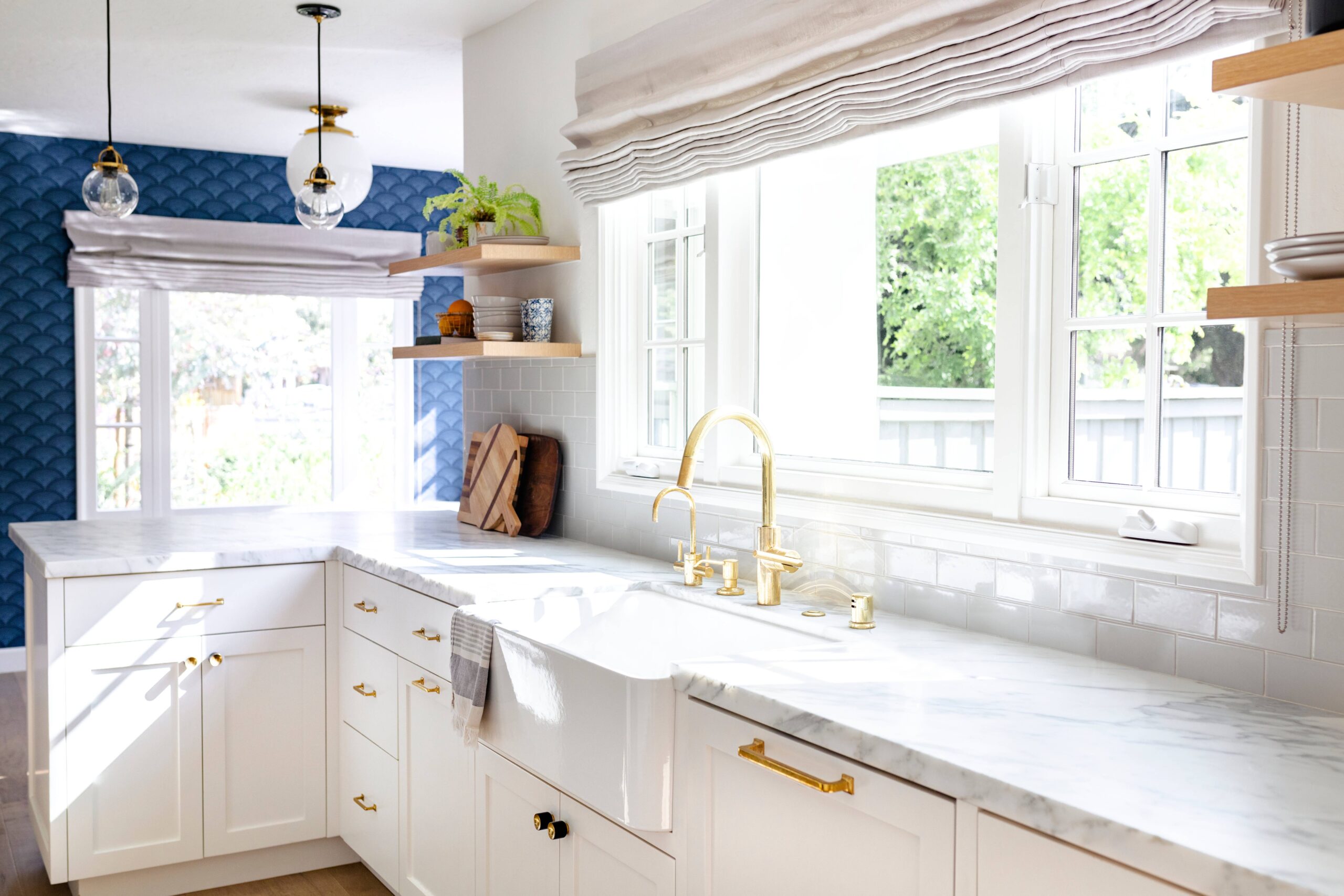 Kitchen with a blue accent wall, white cabinets, gold hardware, and windows with elegant shades at SSignature Shutters and Blinds near Moraine, OH
