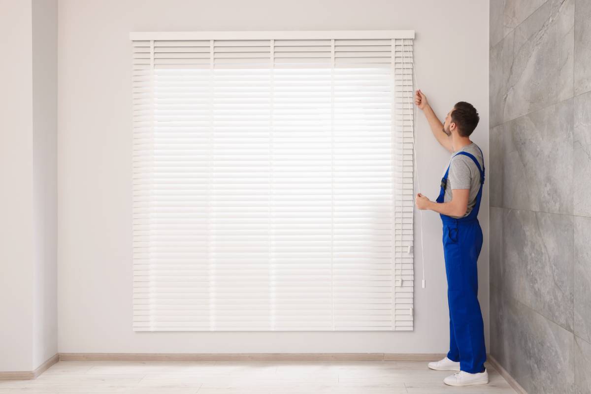 A professional, wearing blue overalls, installing outside mount window treatments in a client’s home at Signature Shutters & Decor near Moraine, OH