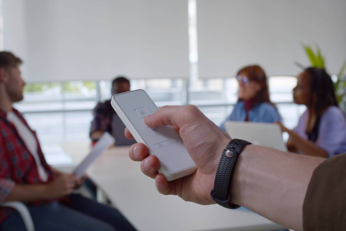 A team member using a remote to close motorized commercial window shades during a meeting